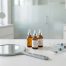 A minimalist medical aesthetic still life featuring skincare serums, a handheld mirror, and syringes in a bright clinic setting